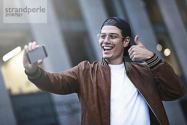 Selfie mania Excited young guy is making selfie on a camera. He is wearing casual trendy wear and snap back