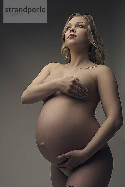 Pregnant naked blonde cropped portrait against gray wall