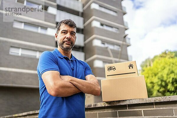 Portrait of a confident delivery man in blue uniform standing with arms crossed looking at camera in the city