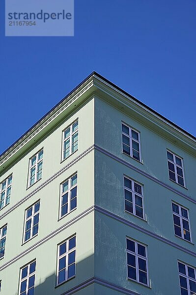 A green corner of a building with many windows against a clear blue sky  Bergen  Vestland  Norway  Europe