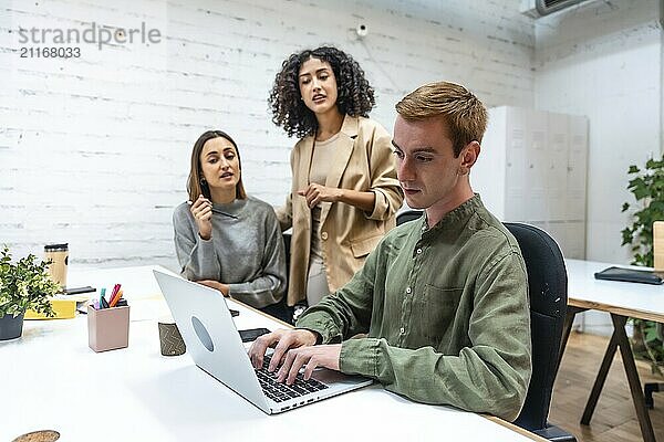 Drei unterschiedliche Kollegen  die in einem Coworking Space über Arbeitsfragen diskutieren und einen Laptop benutzen