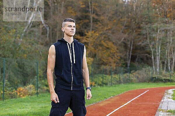 Portrait of a young man jogger in the morning outdoors standing on running race track