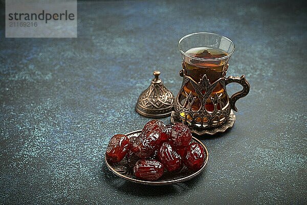 Fastenbrechen mit getrockneten Datteln während des Ramadan Kareem  Iftar Mahlzeit mit Datteln und arabischem Tee im traditionellen Glas  Blickwinkel auf rustikalem blauen Hintergrund. Muslimisches Festmahl  Foodfotografie