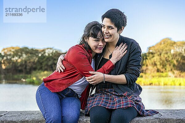 Joyful young couple of women laughing and hugging by the side of a lake