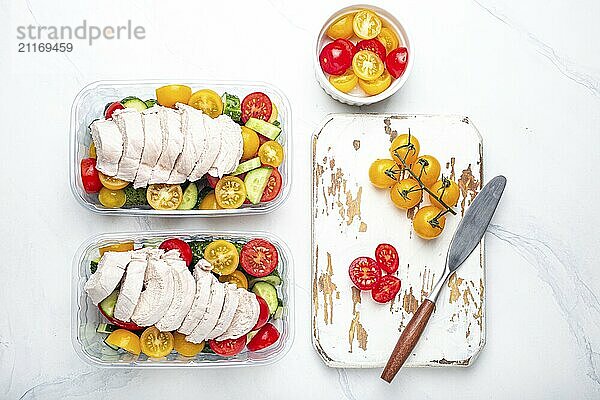 Gesunde Mahlzeit Vorbereitung für das Mittagessen  Diät gekochtes Hühnerfilet mit Gemüse Salat in Lunch Boxen Container Draufsicht auf weißen Marmor Küchentisch Hintergrund mit Messer und Schneidebrett  Lebensmittel Fotografie  food photography  food photography