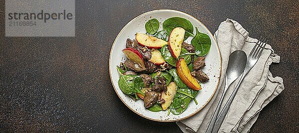 Gesunder Salat mit eisenreichen Zutaten Hühnerleber  Äpfel  frischer Spinat und Walnüsse auf weißem Keramikteller  dunkelbrauner rustikaler Steinhintergrund Draufsicht Kopierraum  Foodfotografie