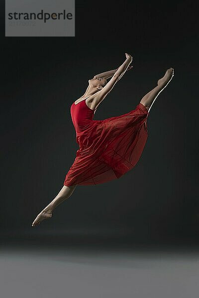 Slim girl wearing red chiffon dress jumping barefoot gracefully in the dark room