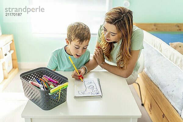 High angle view of a happy mother and boy drawing sitting in the bedroom