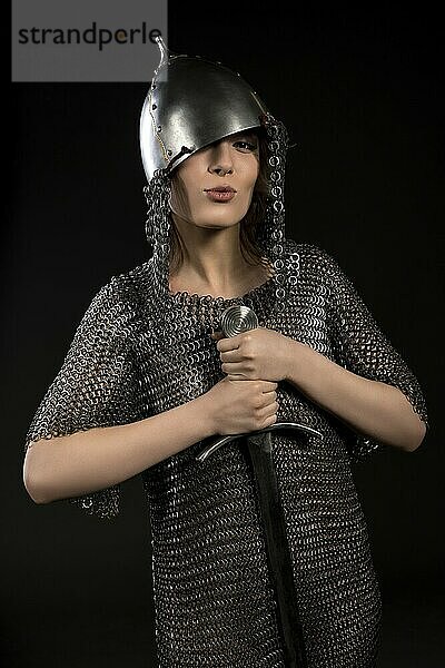 Sexy woman wearing viking helmet and hauberg with a sword isolated view on black background