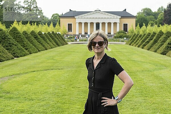 Hübsche dreißigjährige Frau in schwarzem Kleid und Sonnenbrille posiert für den neoklassischen Bontancal Garten und das Gebäude  Uppsala  Schweden  Europa