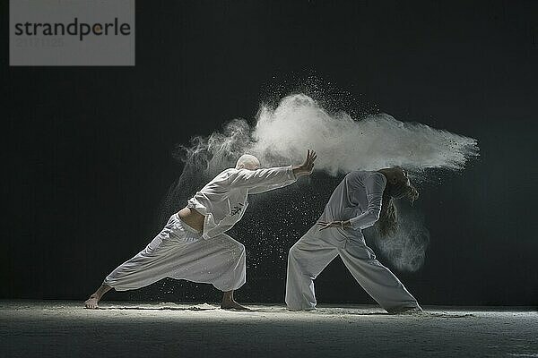 Two male doing yoga in white dust cloud in dark room full-length view