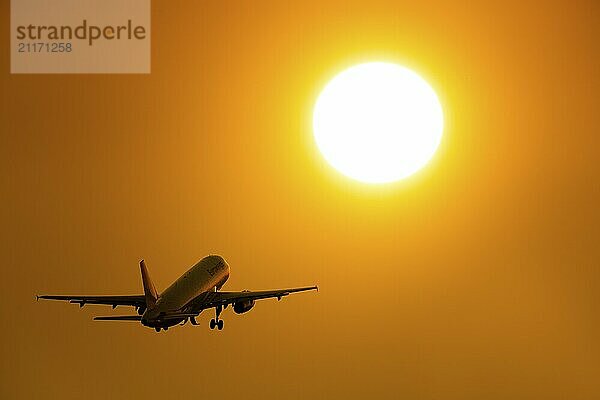 Silhouette eines startenden Flugzeugs vor einem leuchtend orangefarbenen Sonnenuntergang