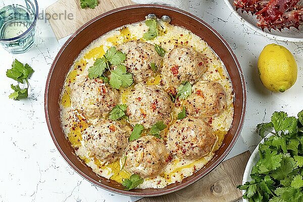 Food  CRABMEATBALLS crab meatballs in white creamy sauce in red pan  whole king crab  cilantro  lemon and white wine on white background