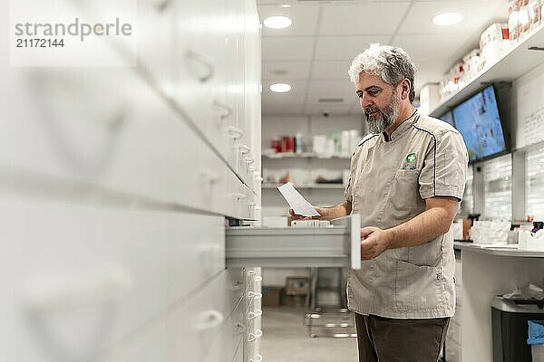 Seitenansicht eines männlichen reifen Apothekers  der im Lagerraum eines Geschäfts nach Medikamenten sucht