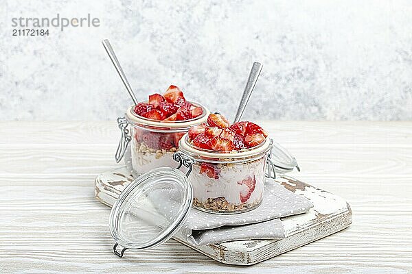 Parfait mit frischen Erdbeeren  Joghurt und knusprigem Müsli in durchsichtigen Einmachgläsern auf weißem  rustikalem Holzhintergrund aus der Vogelperspektive  gesundes Frühstück oder leichtes Sommerfruchtdessert  Foodfotografie  food photography  food photography