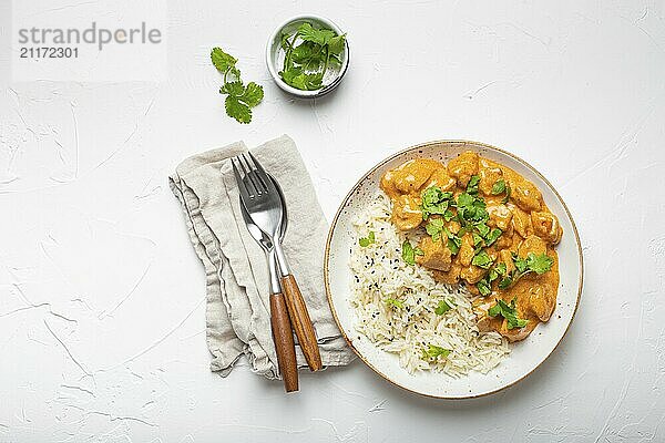 Traditionelles indisches Gericht Hühnercurry mit Basmatireis und frischem Koriander auf rustikalem weißen Teller auf weißem Betontisch Hintergrund von oben. Indisches Abendessen Mahlzeit  Lebensmittel Fotografie  food photography