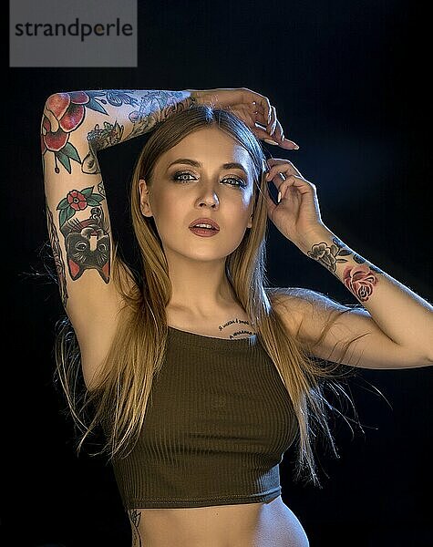 Sexy tattooed blonde in cropped top isolated portrait against black wall