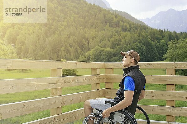 Disabled young man on a wheelchair on a wooden bridge path enjoying in nature looking at beautiful view