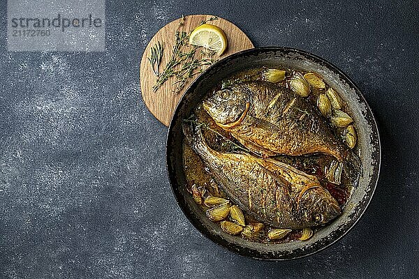 Food  Food  Baked sea bream or dorada with onion and herbs in pan on dark background