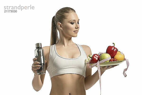 Beautiful fitness trainer holding a plate with friut  a water bottle and a tape-measure cropped isolated view on white background