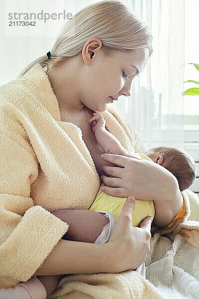 Baby eating breast milk. Caucasian blonde young mother breastfeeding her baby at home vertical photo. Concept of lactation