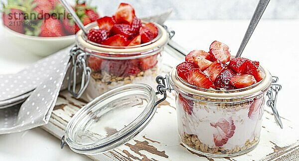 Parfait mit frischen Erdbeeren  Joghurt und knusprigem Müsli in durchsichtigen Einmachgläsern auf weißem  rustikalem Holzhintergrund aus der Vogelperspektive  gesundes Frühstück oder leichtes Sommerfruchtdessert  Foodfotografie