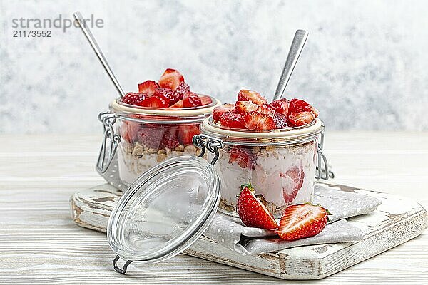 Parfait mit frischen Erdbeeren  Joghurt und knusprigem Müsli in durchsichtigen Einmachgläsern auf weißem  rustikalem Holzhintergrund aus der Vogelperspektive  gesundes Frühstück oder leichtes Sommerfruchtdessert  Foodfotografie