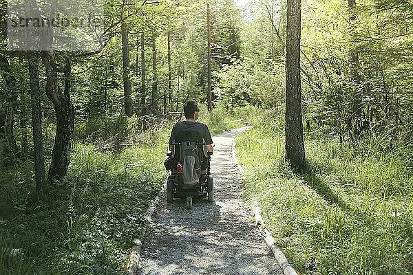 Happy man on wheelchair in nature. Exploring forest wilderness on an accessible dirt path