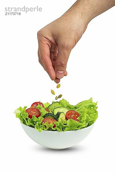 White bowl of salad with fresh cucumbers  tomatoes  iceberg salad leaves and male hand pouring oil with spoon over salad isolated on white background  food photography