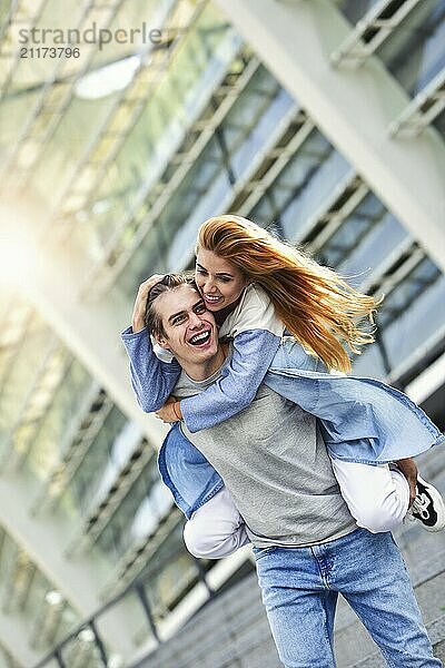 Man giving his pretty girlfriend a piggy back at street smiling at each other on a sunny day