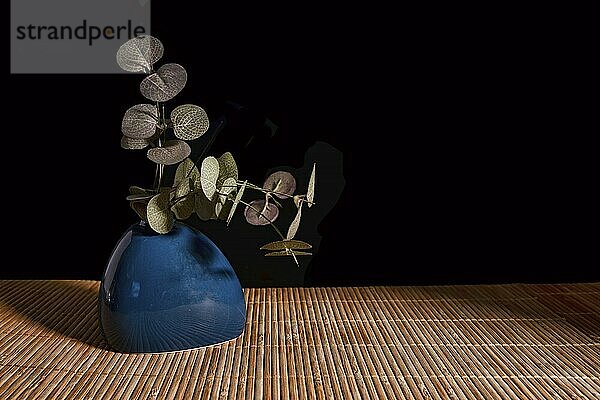 Still life with blue vase  and flower leaves on a dark background with light from the right side