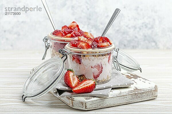 Parfait mit frischen Erdbeeren  Joghurt und knusprigem Müsli in durchsichtigen Einmachgläsern auf weißem  rustikalem Holzhintergrund aus der Vogelperspektive  gesundes Frühstück oder leichtes Sommerfruchtdessert  Foodfotografie