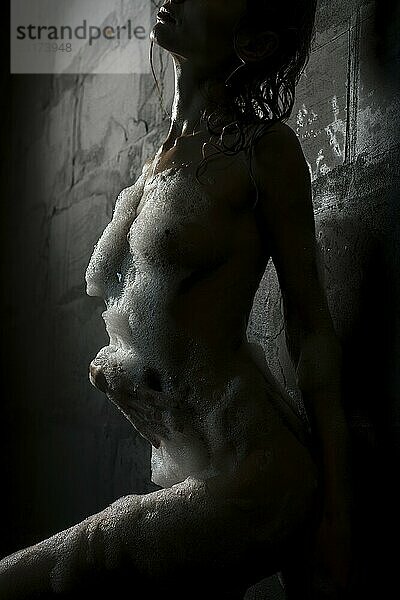 Slim girl in the nude having shower view against brick wall