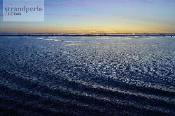 Calm sea under orange blue sky at sunrise with gentle waves  Sunrise  Bergen  Vestland  Norway  Europe