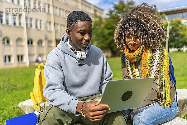 Two male and female multiraical students sitting with laptop on a bench at campus