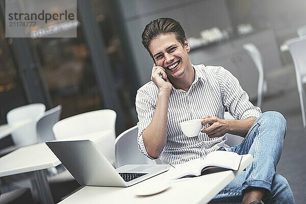 Handsome caucasian young man with phone working on laptop and smiling while enjoying coffee in cafe