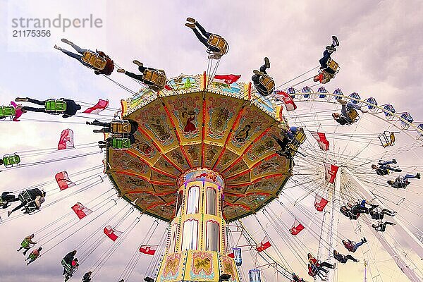 Kettenkarussell in Bewegung mit fröhlichen Menschen vor wolkigem Himmel  Riesenrad  Wellenflug  Cannstadter Volksfest  Stuttgart  Baden-Württemberg