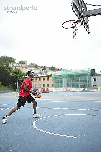 Vertical full length of an african american basketball player training along in an urban court