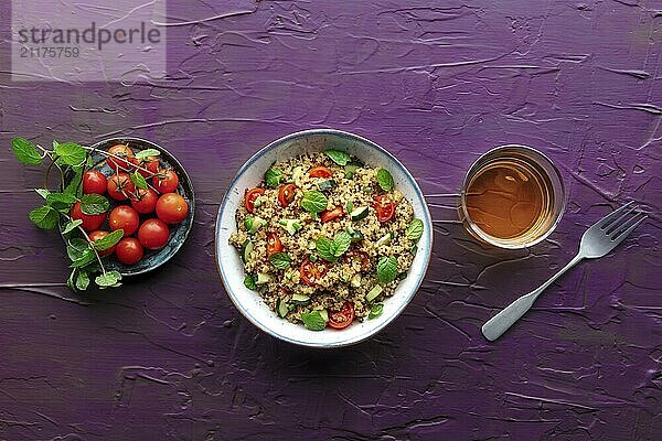 Quinoa Tabbouleh Salat in einer Schüssel  ein gesundes Abendessen mit Tomaten und Minze  Overhead Flat Lay Aufnahme auf einem lila Hintergrund mit Kopierraum  Food Fotografie