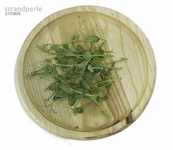 Shoots of young green pea microgreens in a wooden bowl  top view of tasty and healthy plants isolated on white background