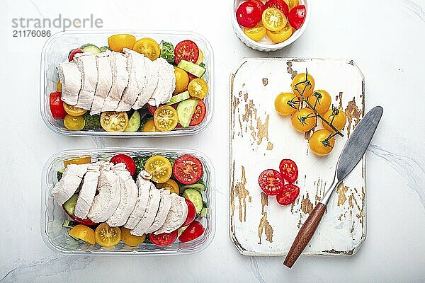 Gesunde Mahlzeit Vorbereitung für das Mittagessen  Diät gekochtes Hühnerfilet mit Gemüse Salat in Lunch Boxen Container Draufsicht auf weißen Marmor Küchentisch Hintergrund mit Messer und Schneidebrett  Lebensmittel Fotografie  food photography