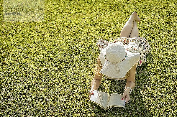 Pretty woman reading book lying on the lawn  seen from above with summer hat