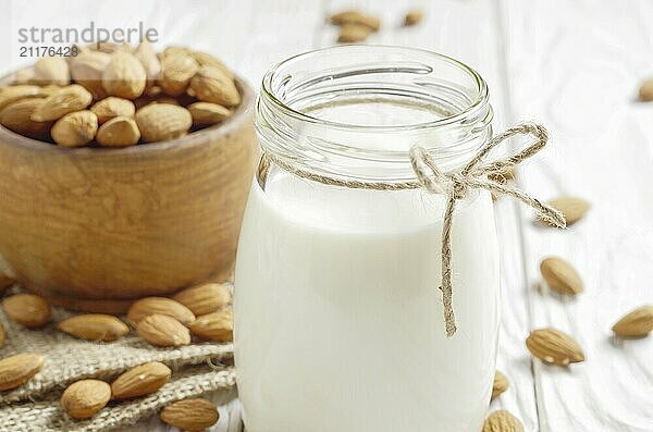 Milk or yogurt in mason jar on white wooden table with bowl of almonds on hemp napkin aside