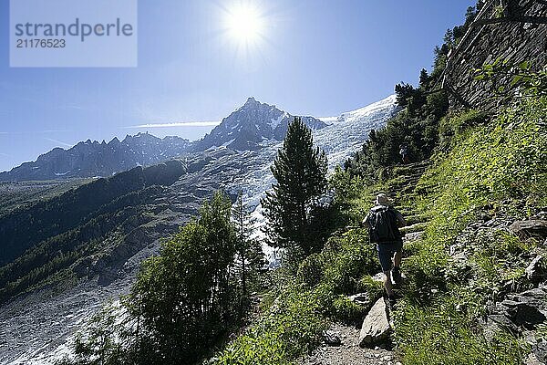 Hiker on hiking trail La Jonction  view of glacier Glacier des Bossons with sun star  behind summit of Aiguille du Midi  Chamonix  Haute-Savoie  France  Europe