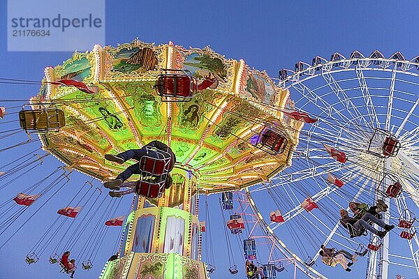 Beleuchtetes Kettenkarussell und Riesenrad bei Nacht mit fröhlichen Menschen  Jahrmarkt  Wellenflug  Cannstadter Volksfest  Stuttgart-Bad Cannstsdt  Baden-Württemberg