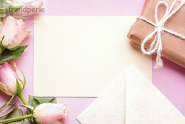 Gifting theme image with a blank paper in the middle  surrounded by lovely pink roses  an envelope and a gift box wrapped in brown paper  on a pink background