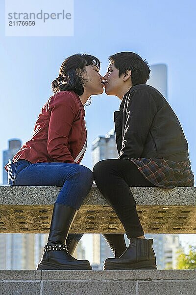 Romantic low-angle view of a young couple of women sharing a kiss on a park bench