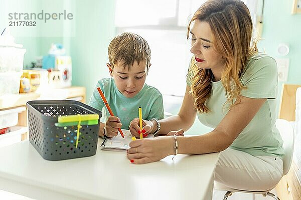 Happy and tender scene of a mother and school boy coloring at home together