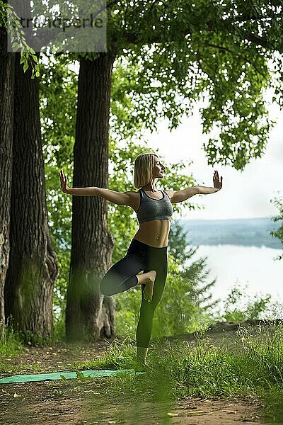 Young girl doing yoga on a summer forest glade on high river bank shot