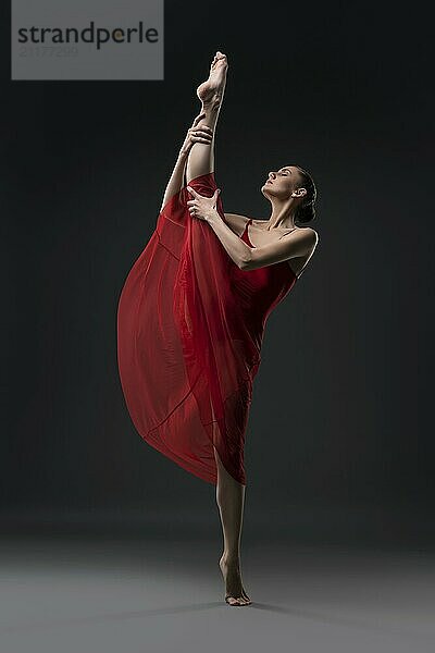 Pretty girl wearing red chiffon dress dancing barefoot in the dark room